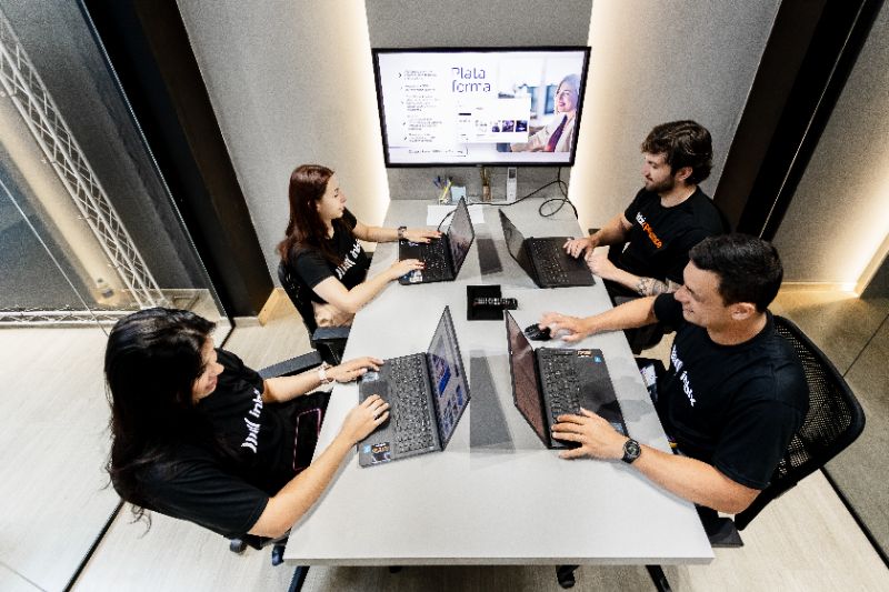 Equipe diversa reunida em ambiente corporativo moderno, discutindo e trocando ideias com laptops e documentos