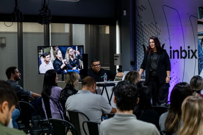 Colaboradores em ambiente corporativo moderno assistindo treinamento em sala com laptop e tela digital