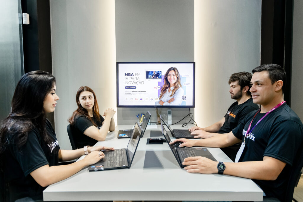 Tela de computador exibindo motion graphics em treinamento corporativo com pessoas assistindo em escritório moderno