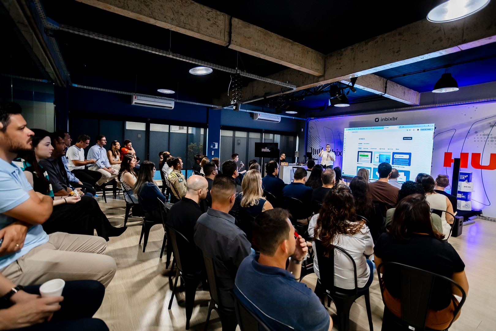 Líder de vendas em pé diante de telão com dados de IA em ambiente de treinamento corporativo